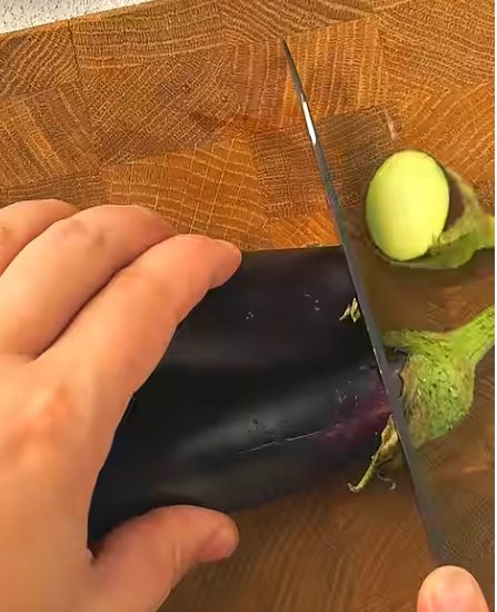 Cutting fresh eggplant on a wooden board to prepare Crispy Eggplant Salad