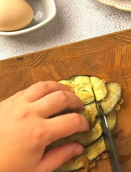 Slicing fried eggplant for Crispy Eggplant Salad on a wooden cutting board